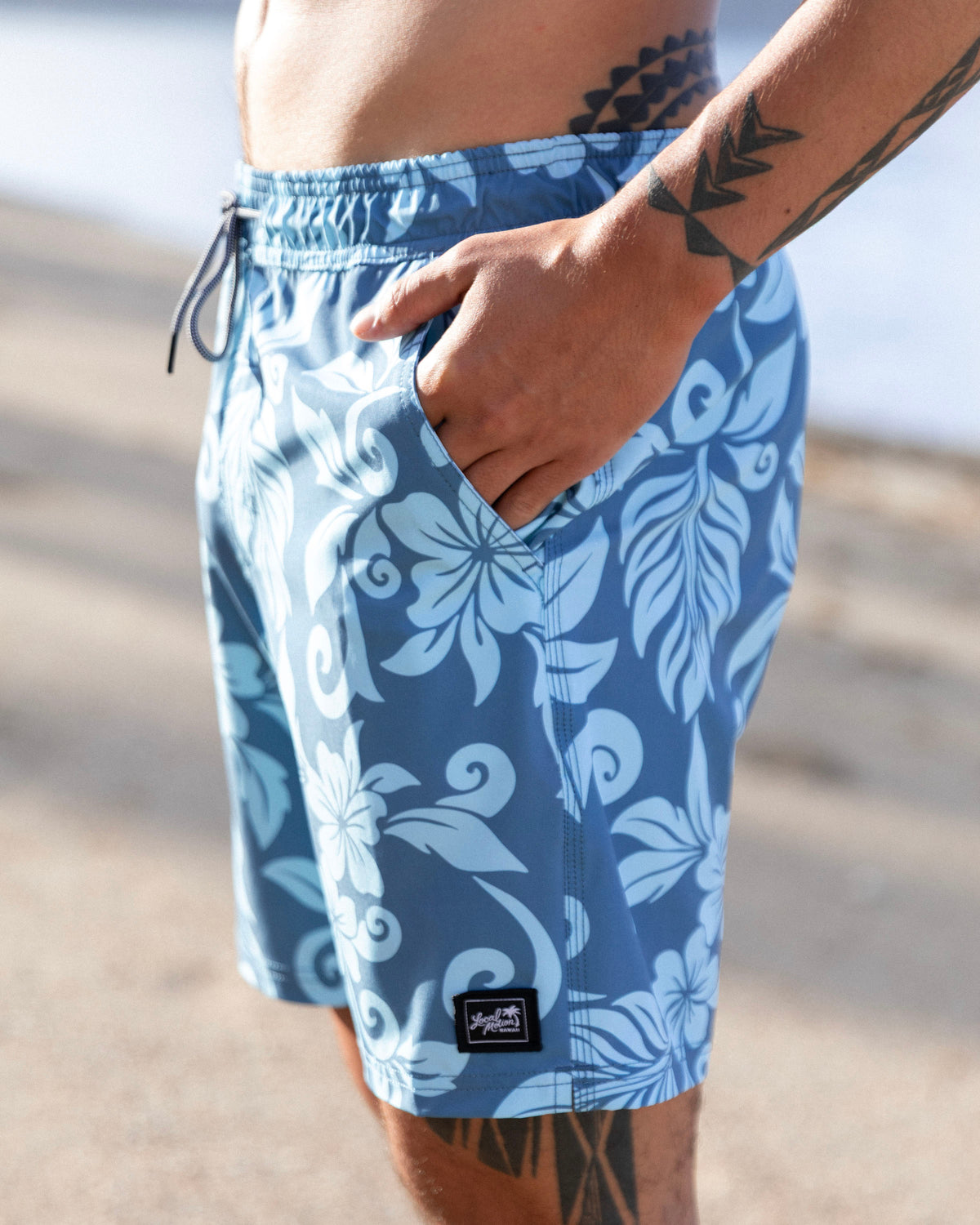 A close-up of a person wearing blue swim trunks with a white floral pattern [pacific blue]