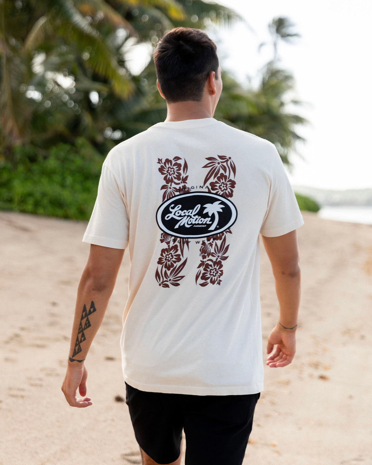 A man walking on a sandy beach seen from behind, wearing a cream-colored t-shirt [parchment]