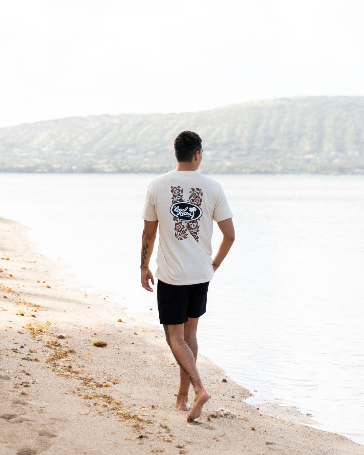 A man walking on a sandy beach next to the water, viewed from behind. [parchment]