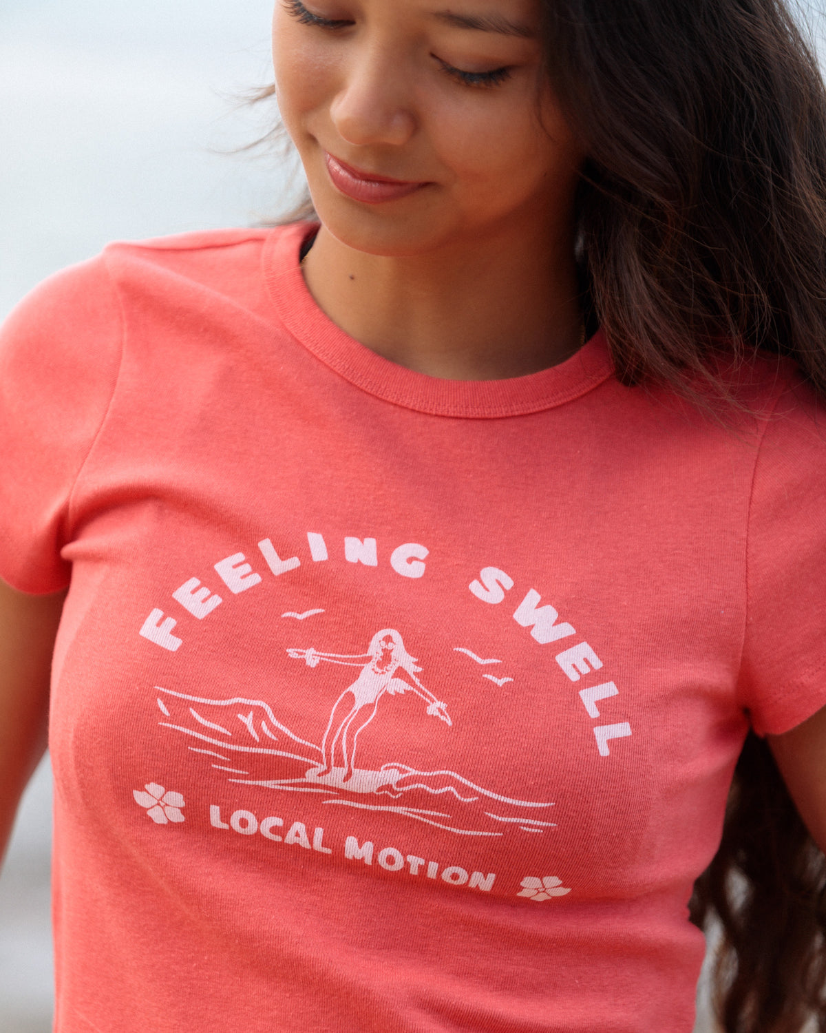 Woman wearing a red graphic shirt that reads 'FEELING SWELL' [rust red]