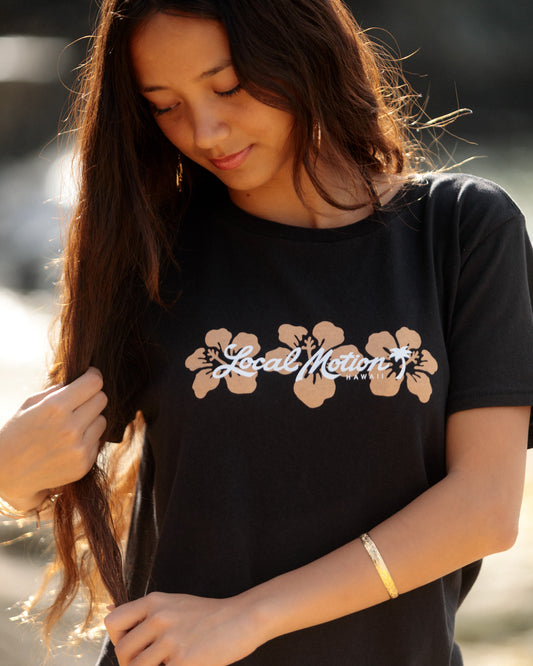 A woman wearing a black t-shirt with a graphic of tan hibiscus flowers [black]